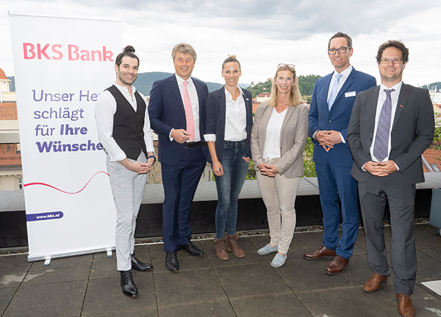 Sechs Personen sind am Bild und lachen in die Kamera. Am Plakat steht der Slogan der BKS Bank „Unser Herz schlägt für Ihre Wünsche“.